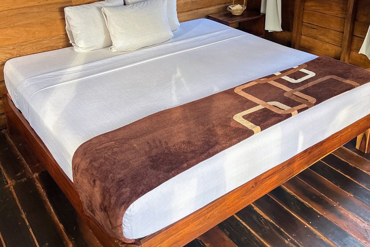 Una habitación de cabaña de madera con cama, un tapiz tejido en la pared y una ventana con cortinas.