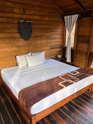 Una habitación de cabaña de madera con cama, un tapiz tejido en la pared y una ventana con cortinas.