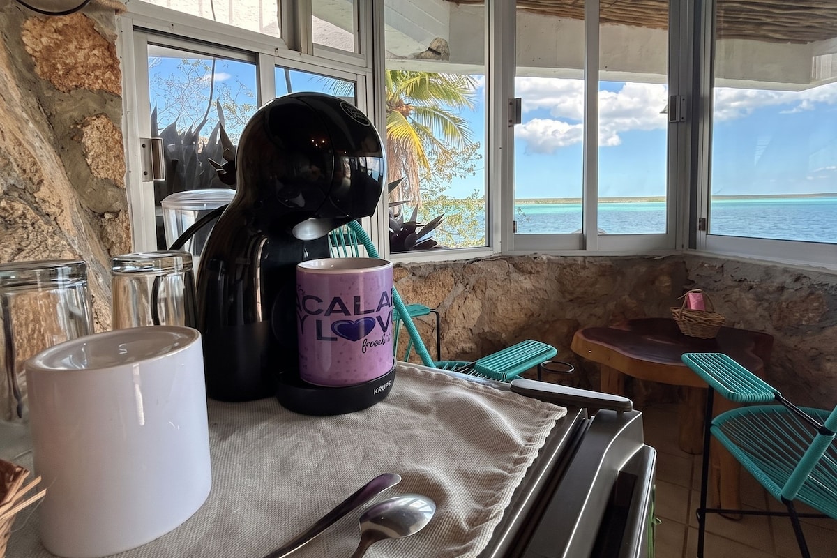 Un comedor con una mesa preparada para dos personas, una cafetera, una taza y un casco.