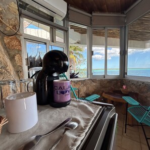 Un comedor con una mesa preparada para dos personas, una cafetera, una taza y un casco.