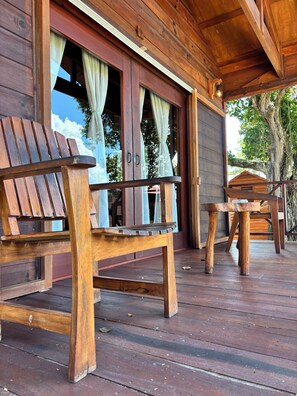 A wooden deck with a wooden chair and table, a wooden building with a window, and a tree in the background. - Hotel My Love Bacalar Lagoon Front - Free Kayak Rental (Bacalar)