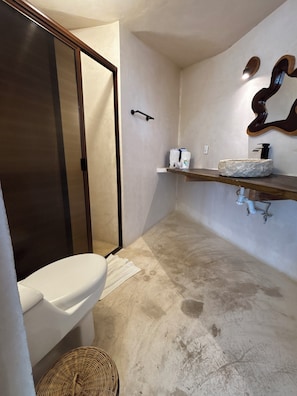 Un baño con inodoro, ducha, lavabo de piedra y un perchero para toallas.