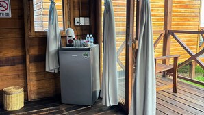 Una cabaña de madera con un refrigerador pequeño, una cesta y una mesa con un banco.