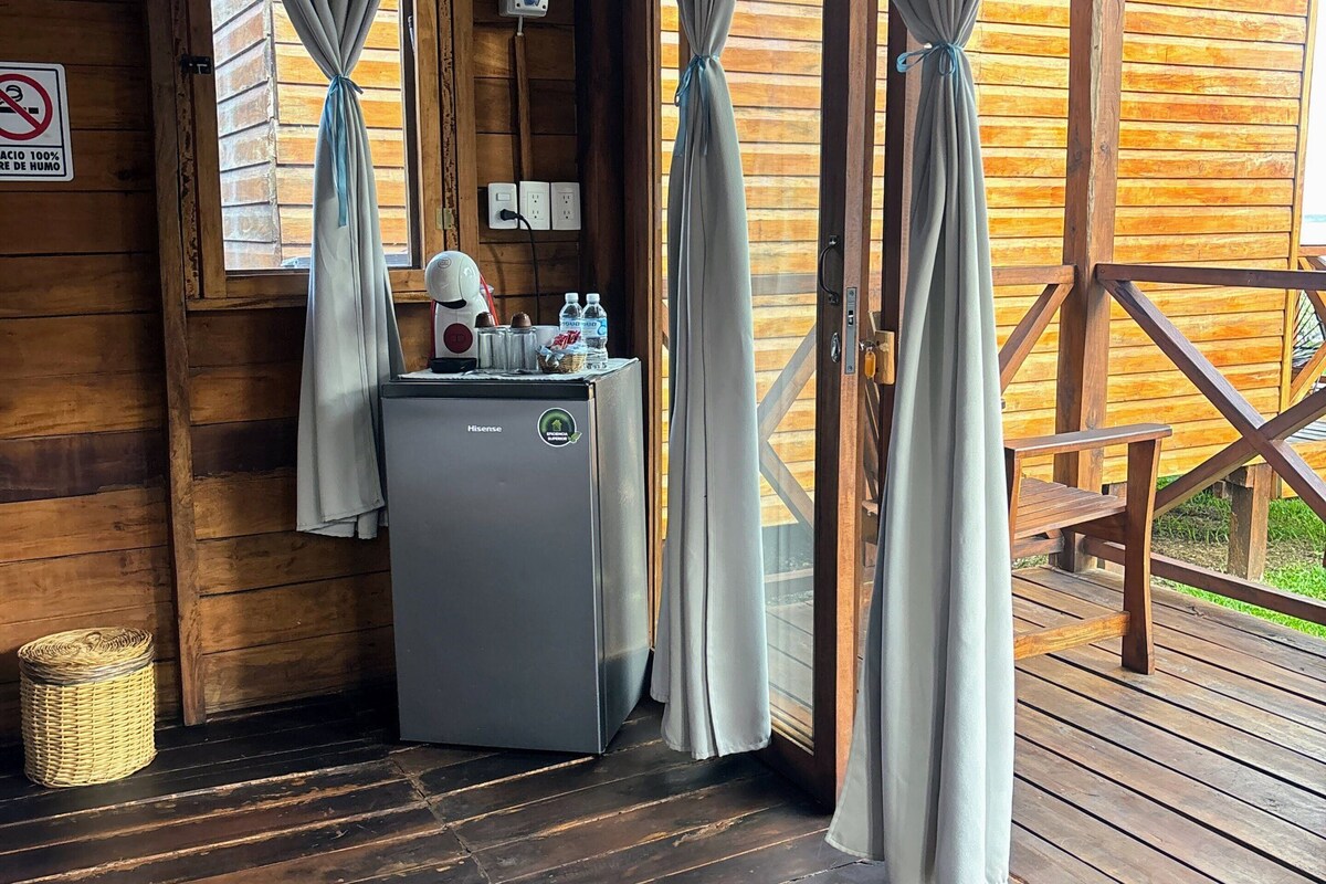 Una cabaña de madera con un refrigerador pequeño, una cesta y una mesa con un banco.