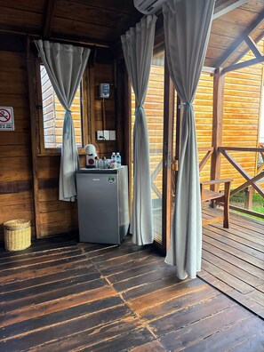 Una cabaña de madera con un refrigerador pequeño, una cesta y una mesa con un banco.