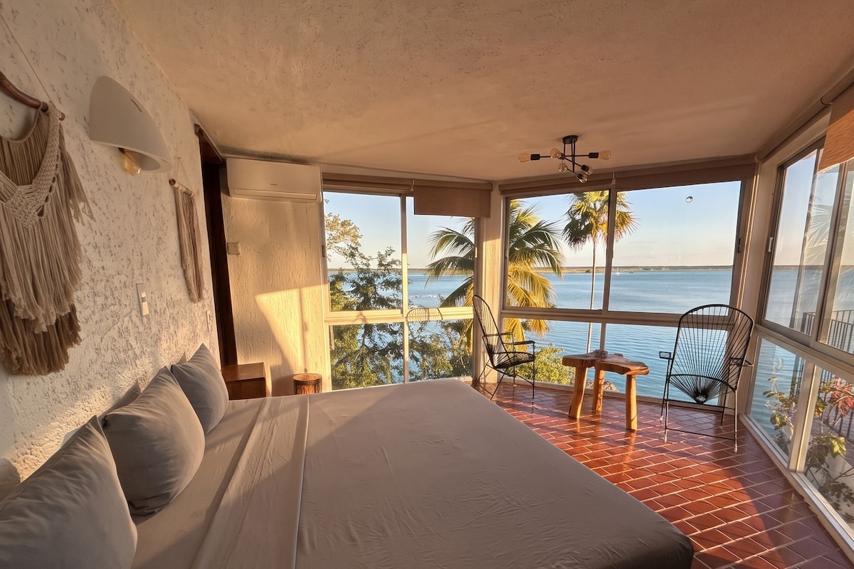 Ein Schlafzimmer mit einem großen Bett, Meerblick und einem Balkon mit Sitzgelegenheiten.