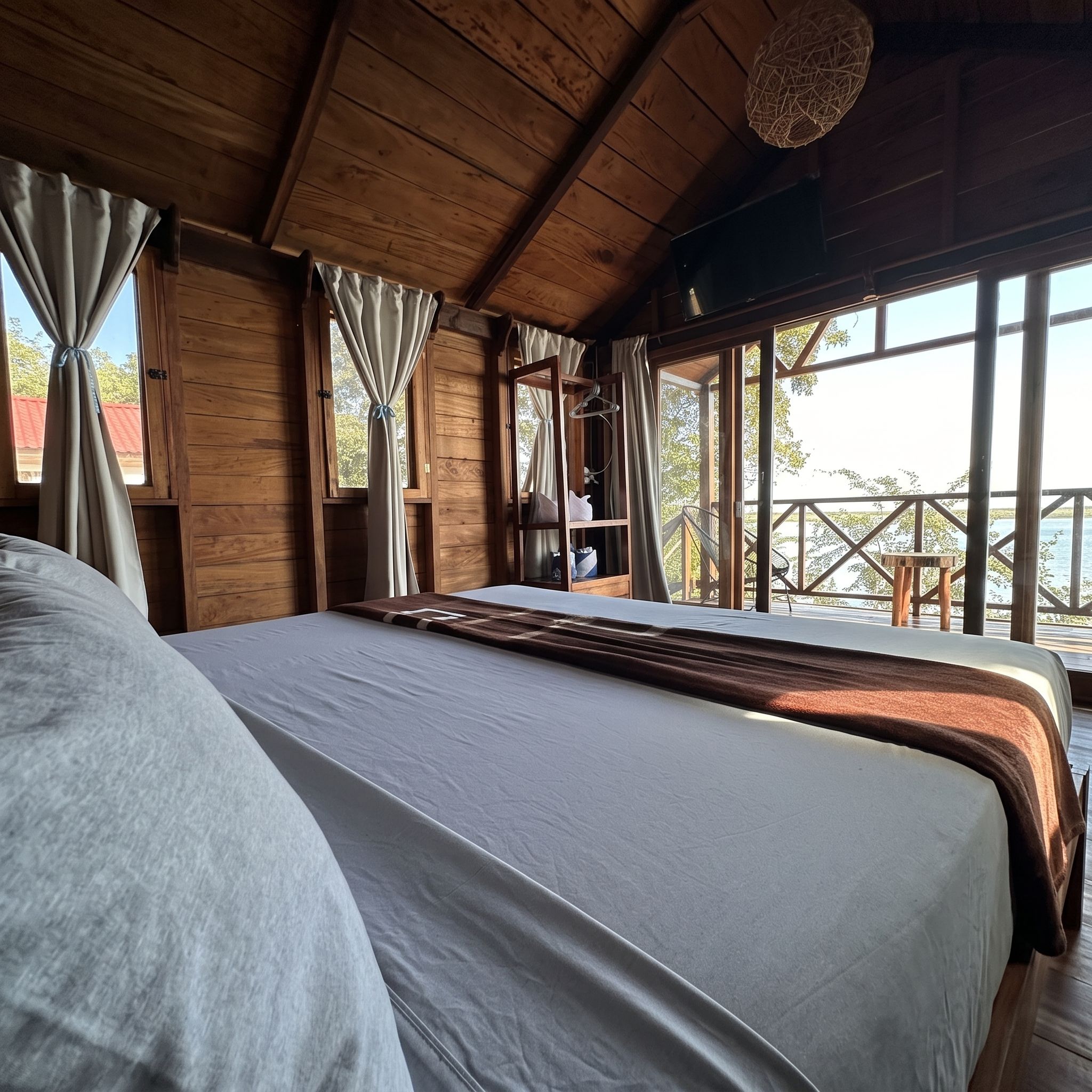 Un dormitorio de cabaña de madera con una cama grande, cortinas y vistas al exterior.