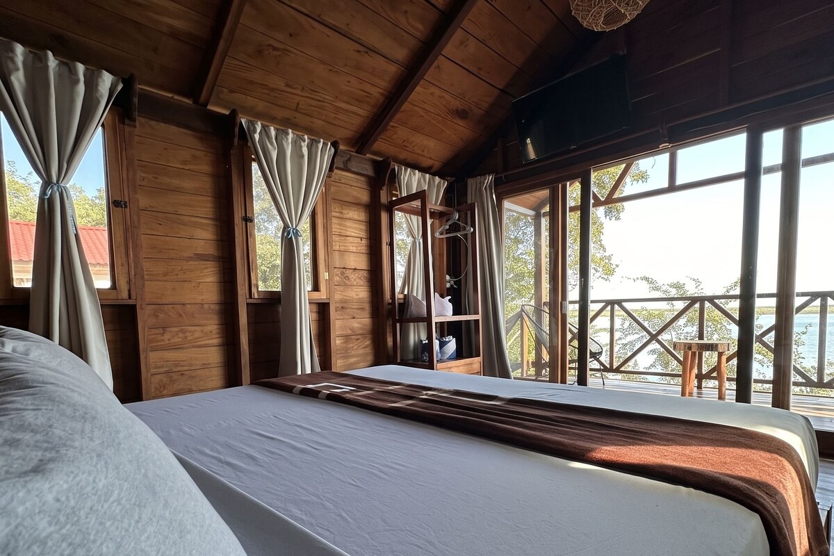 Un dormitorio de cabaña de madera con una cama grande, cortinas y vistas al exterior.