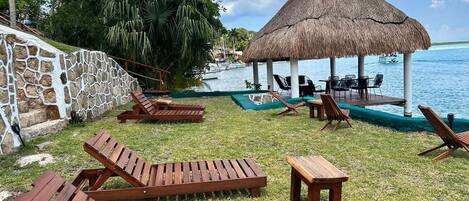 Un entorno de resort tropical con sillones de madera y una estructura de techo de paja junto al agua.