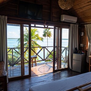 Una habitación con terraza de madera, cama, televisor y aire acondicionado.