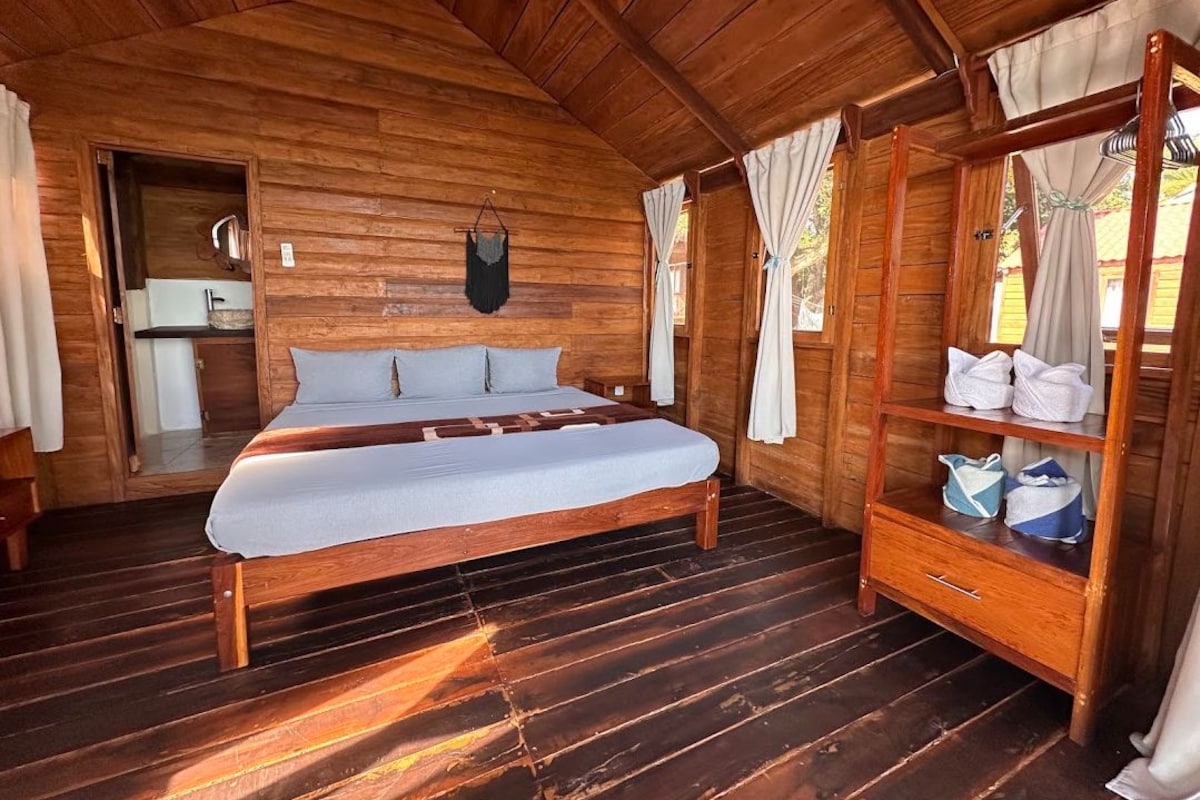Un dormitorio de cabaña de madera con cama, armario y una pequeña cocina.