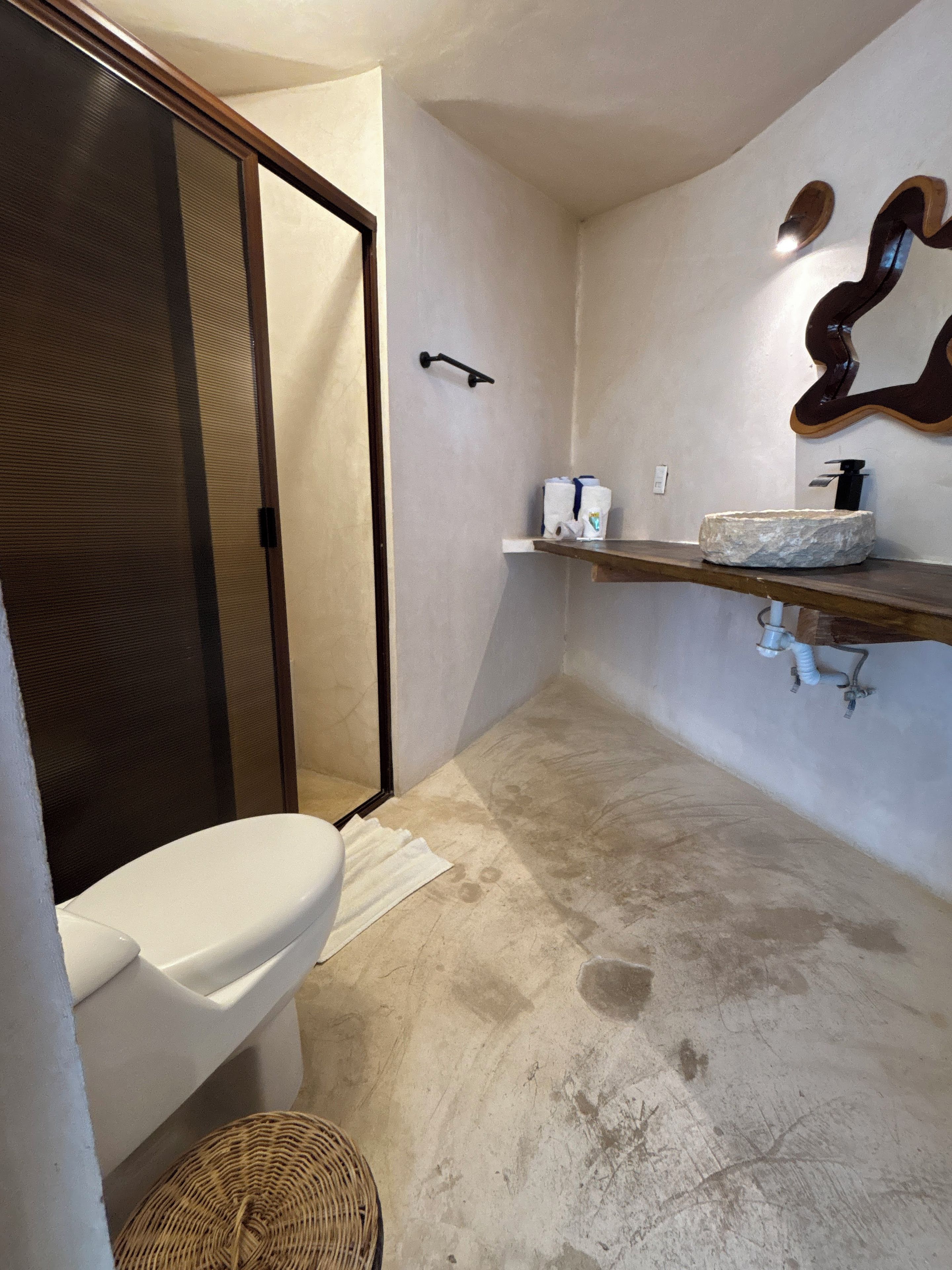 A bathroom with a toilet, a shower, a sink with a stone basin, and a towel rack.