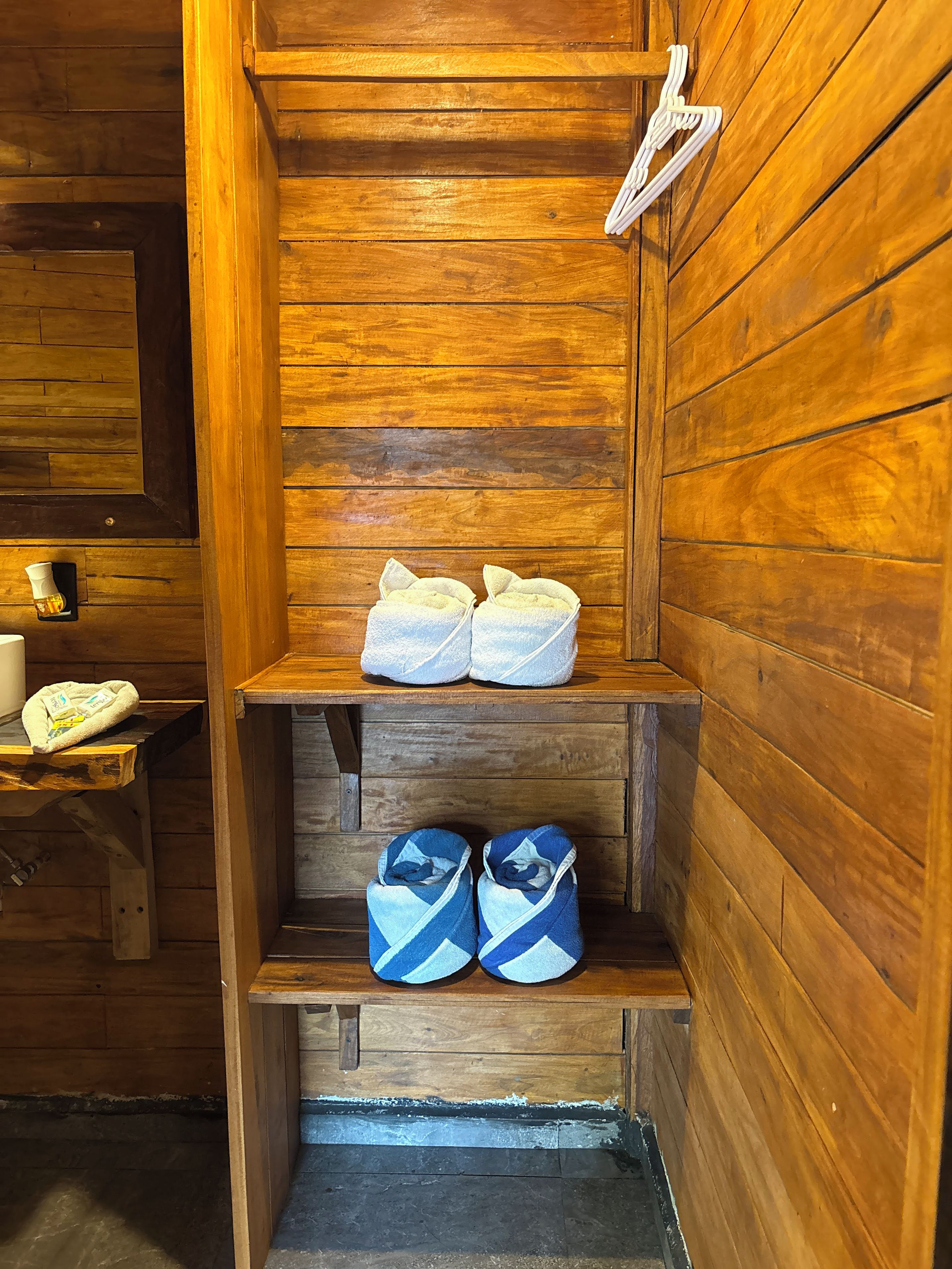 A wooden interior with a shelf holding towels and a bench with bags.