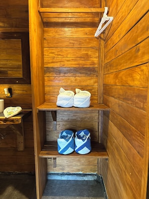 A wooden interior with a shelf holding towels and a bench with bags.