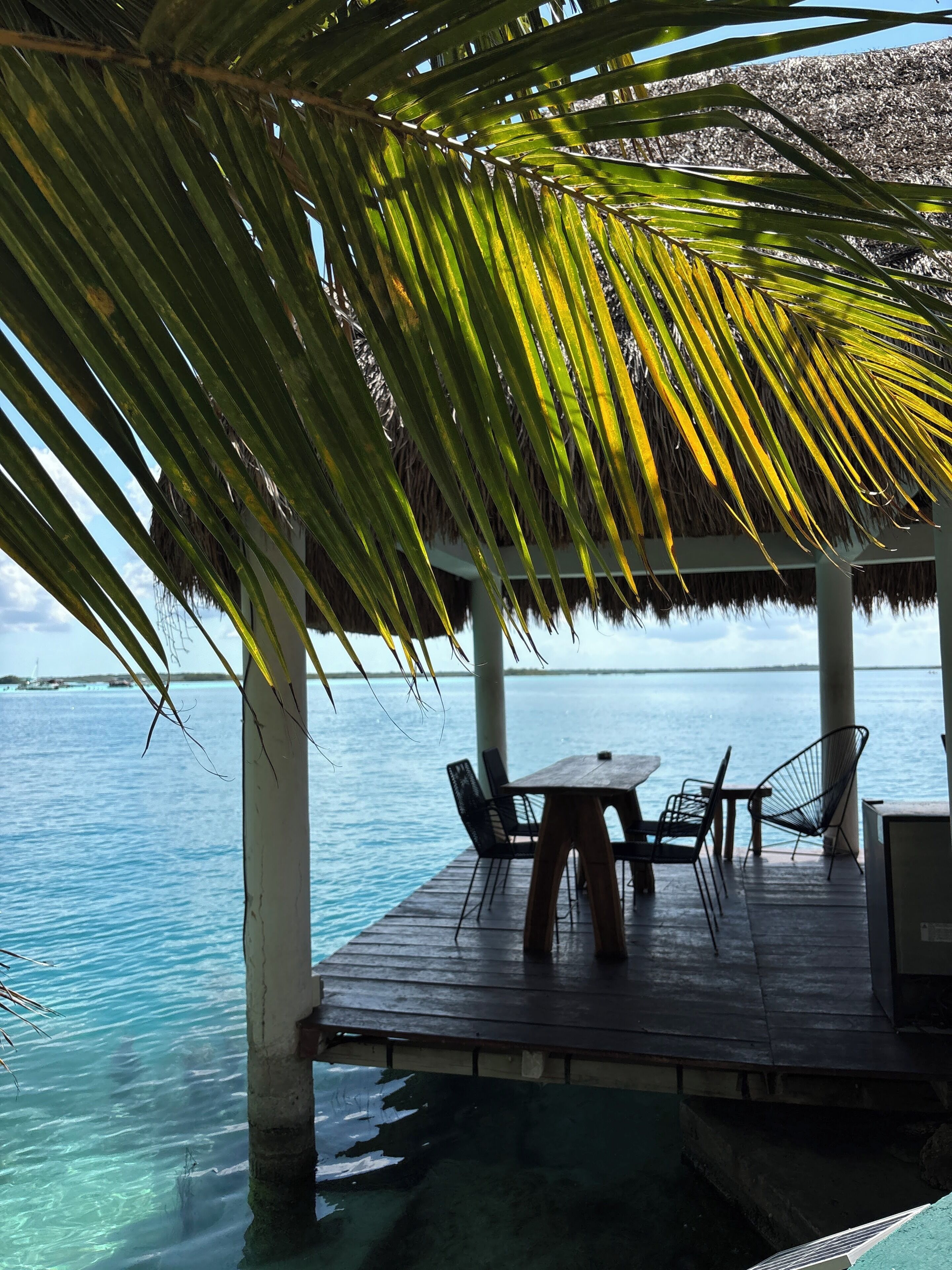 A wooden deck with a table and chairs overlooking clear blue water.