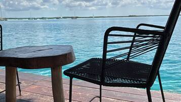 A wooden table and a metal chair on a wooden deck overlooking a body of water with sailboats.