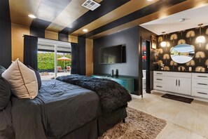 Ein Schlafzimmer mit Bett, Fernseher, Schreibtisch und einem Badezimmer mit Spiegel und Beleuchtung.