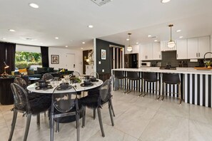 Une cuisine moderne avec des meubles blancs, un îlot central doté de tabourets et un coin repas avec une table ronde et des chaises.