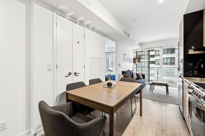 Eine moderne Küche mit Einbauherd, eine Essecke mit Holztisch und Stühlen sowie ein Blick auf die Stadt durch große Fenster.