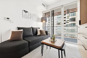 Una sala moderna con un sofá negro, una mesita de madera y un ventanal con vistas a un edificio.