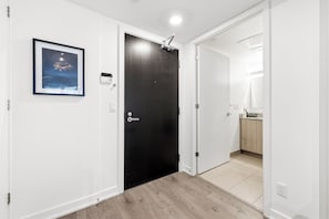 Un pasillo con una puerta negra, un cuadro en la pared y un baño a la vista a través de una puerta abierta.