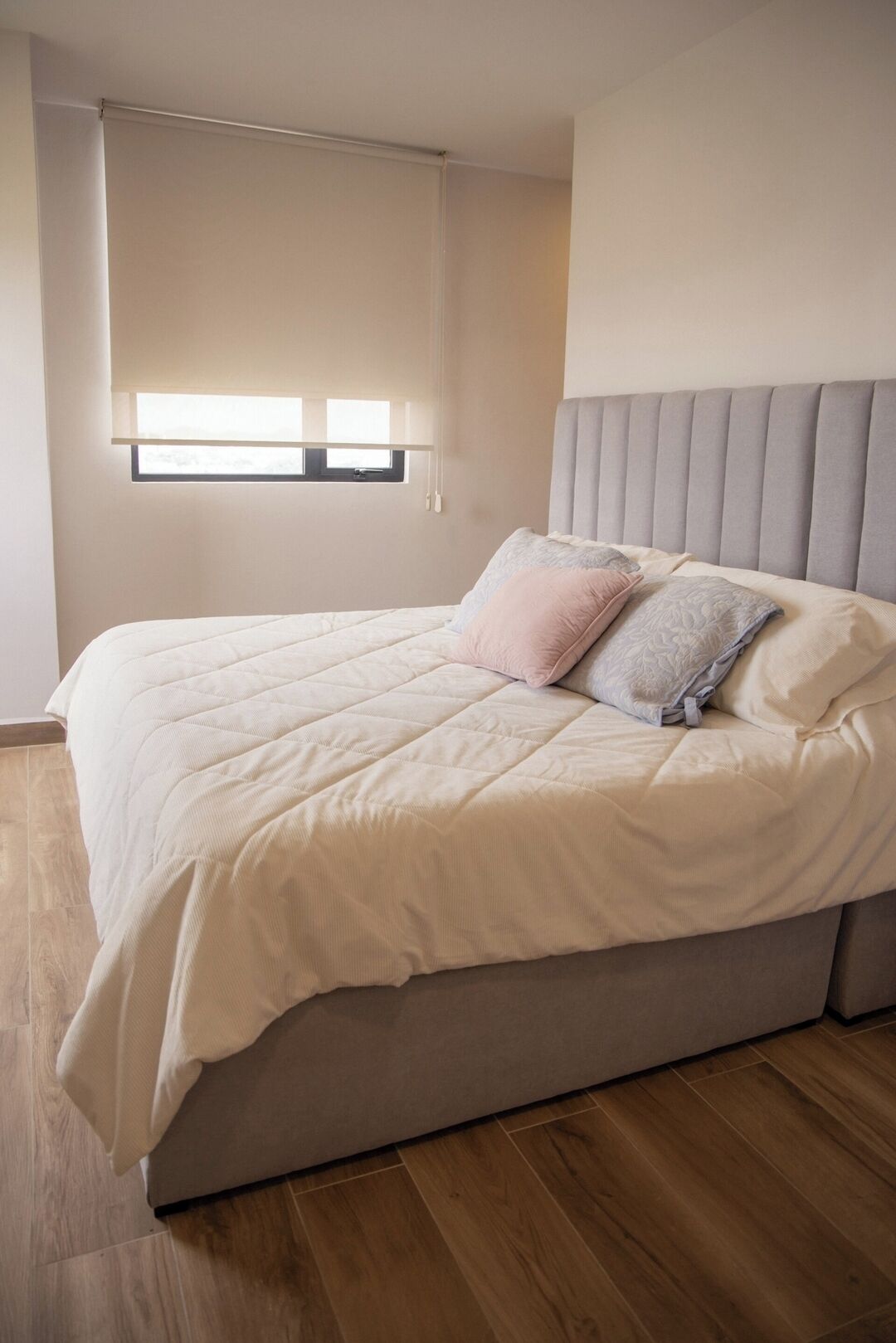 Un dormitorio con una cama, cabecera, ventana con persianas y suelo de madera.