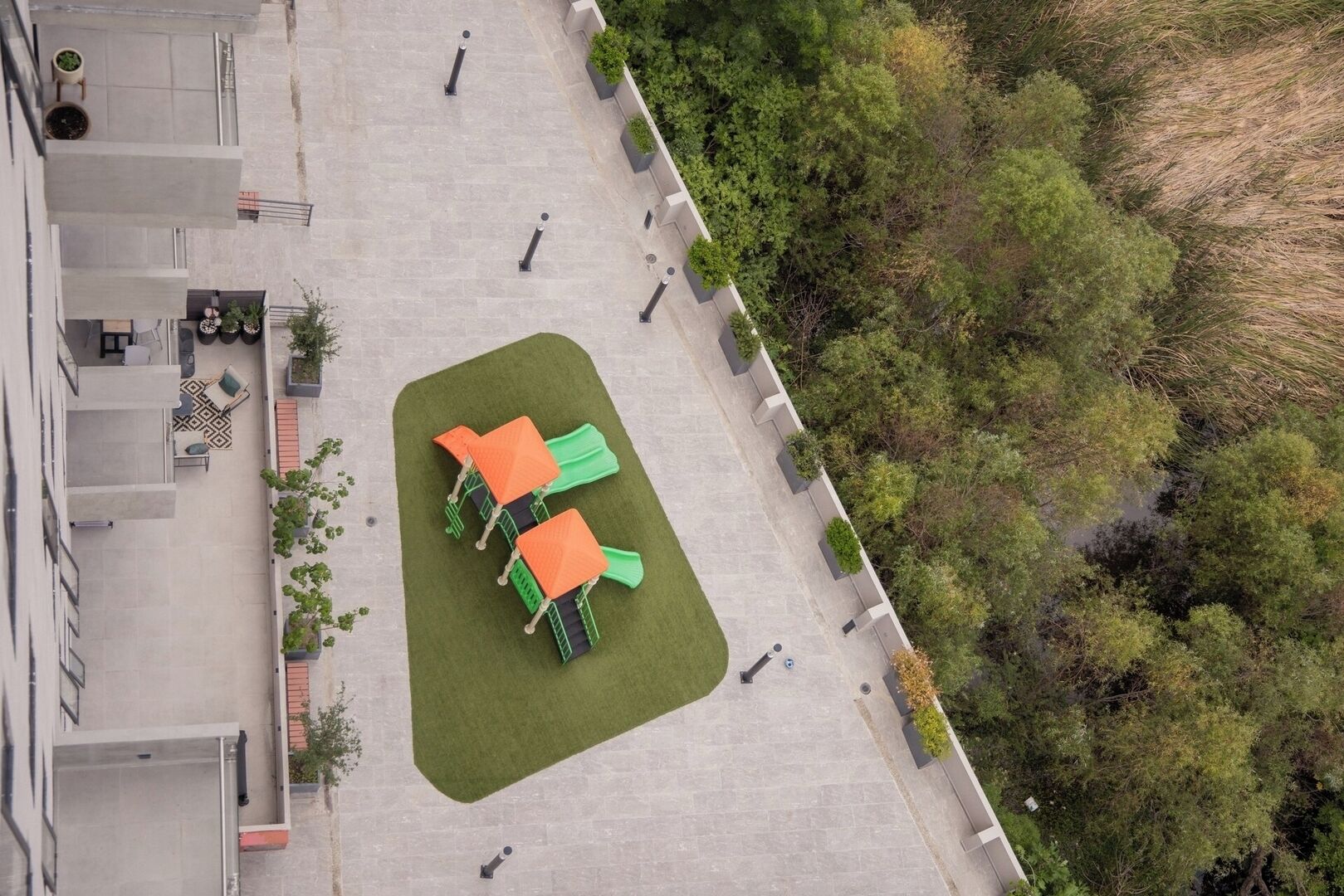 Vista aérea de un patio con césped verde, dos mesas naranjas y abundante vegetación circundante.