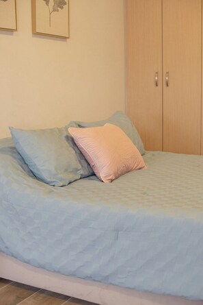 A bed with a blue quilt and two pillows, a wooden wardrobe, and a wall with framed artwork. - Elegant 2-Bedroom Condo in Colomos, Providencia (Guadalajara)