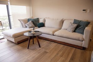 A modern living room with a sectional sofa, a round coffee table, and a view of the outdoors. - Elegant 2-Bedroom Condo in Colomos, Providencia (Guadalajara)