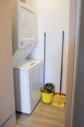 A laundry room with a washing machine, a mop, and a broom. - Elegant 2-Bedroom Condo in Colomos, Providencia (Guadalajara)