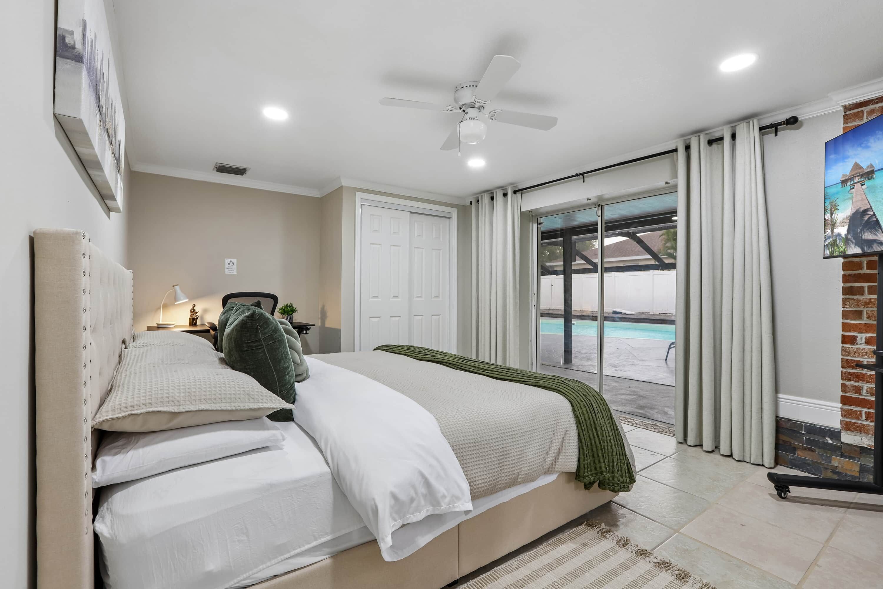 Une chambre avec un lit, un ventilateur de plafond, une vue sur une piscine et une porte donnant sur un espace extérieur.