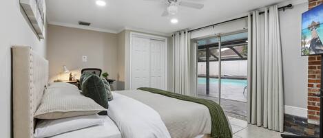 Une chambre avec un lit, un ventilateur de plafond, une vue sur une piscine et une porte donnant sur un espace extérieur.
