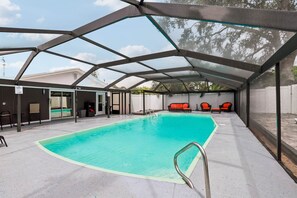 A covered swimming pool with a metal frame, a pool ladder, and a lounge area with red chairs. - Pool, Mini Golf, Pool Table, Fire Pit, Sleeps 10 (Pinellas County)
