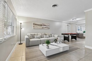 A modern living room with a sofa, coffee table, and a pool table. - Pool, Mini Golf, Pool Table, Fire Pit, Sleeps 10 (Pinellas County)