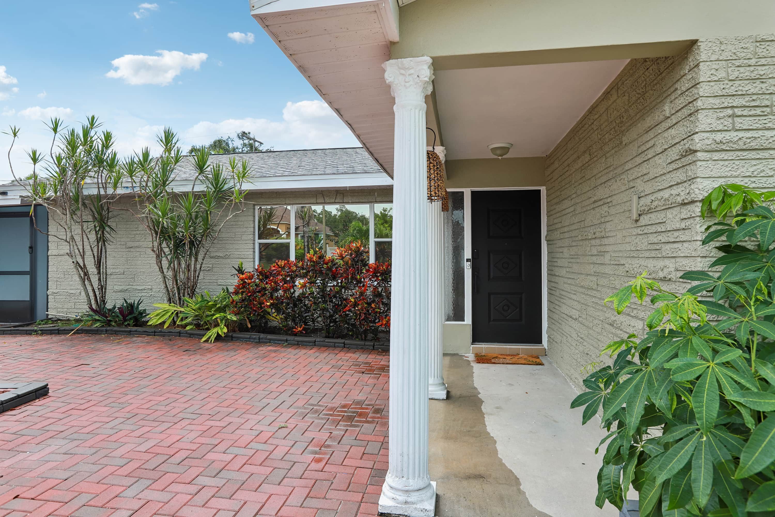 A house with a brick driveway, a white porch column, and a door with a black door frame.