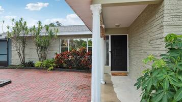 A house with a brick driveway, a white porch column, and a door with a black door frame.