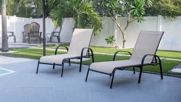 Two lounge chairs with a metal frame and a beige cushion, placed on a paved patio area.