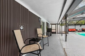 Ein überdachter Außenbereich mit Sitzgelegenheiten, zwei Stühlen, einem Tisch, einem Pool und Blick ins Freie.