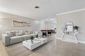 A modern living room with a sofa, coffee table, and a pool table. - Pool, Mini Golf, Pool Table, Fire Pit, Sleeps 10 (Pinellas County)