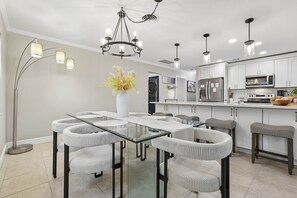 A modern kitchen with white cabinets, stainless steel appliances, and a dining area with a glass table and upholstered chairs. - Pool, Mini Golf, Pool Table, Fire Pit, Sleeps 10 (Pinellas County)