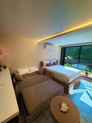 Ein modernes Schlafzimmer mit Schlafsofa, einem separaten Bett, einem kleinen runden Tisch und Blick auf Grün hinter großen Fenstern.