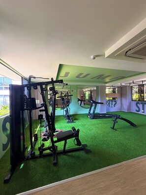 A gym with exercise equipment, a treadmill, and a green artificial turf floor. - ApartaEstudio Pance - Wifi y Coworking (Cali)