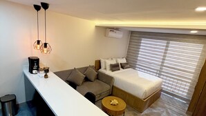 A modern hotel room with a white desk, a sofa, a bed, and a round wooden side table. - ApartaEstudio Pance - Wifi y Coworking (Cali)