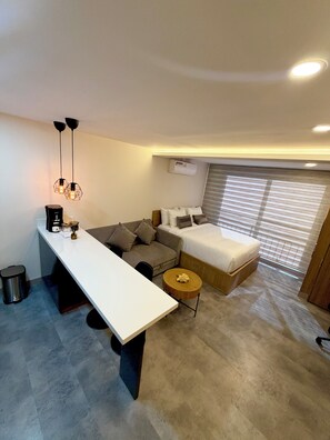 A modern hotel room with a white desk, a sofa, a bed, and a round wooden side table. - ApartaEstudio Pance - Wifi y Coworking (Cali)