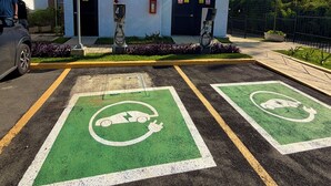 A parking area with electric vehicle charging stations, a building with multiple garage doors, and a clear blue sky. - ApartaEstudio Pance - Wifi y Coworking (Cali)