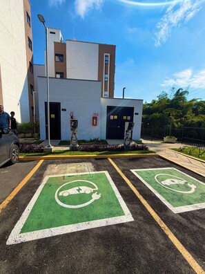 A parking area with electric vehicle charging stations, a building with multiple garage doors, and a clear blue sky. - ApartaEstudio Pance - Wifi y Coworking (Cali)