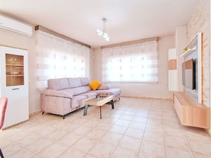 Ein Wohnzimmer mit einer Couch, einem Couchtisch, einem Fernseher und einem Fenster mit Jalousien.
