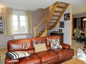 A brown leather sofa with striped and geometric pillows, a wooden staircase, and a dining area with striped chairs. - Gîte La Grenouillère by Interhome (Esquéhéries)