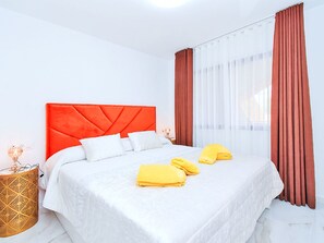 Ein Hotelzimmer mit einem großen Bett, weißer Bettwäsche, einem roten Kopfteil und einem Fenster mit Vorhängen.