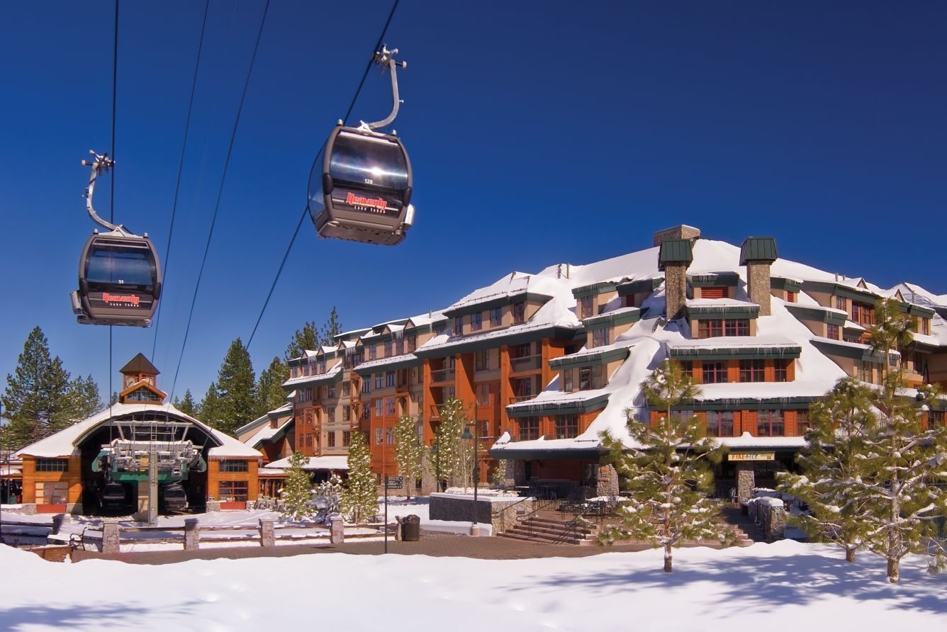A snow-covered lodge with a ski lift, wooden architecture, and a clear blue sky.